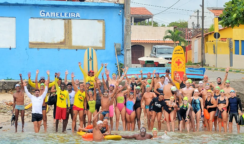 Grupo de nadadores e voluntários de braços erguidos, comemorando na areia da praia.
