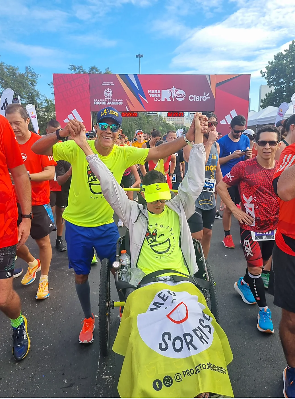 Corredores de braços erguidos na Maratona do Rio, com uma cadeira coberta por uma manta com a marca Meu Sorriso.