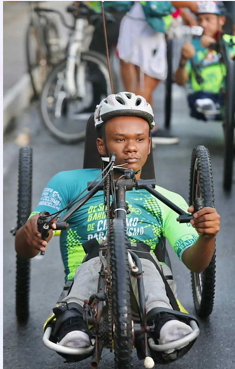 Atleta de capacete e camisa verde pedala uma handbike, de frente.