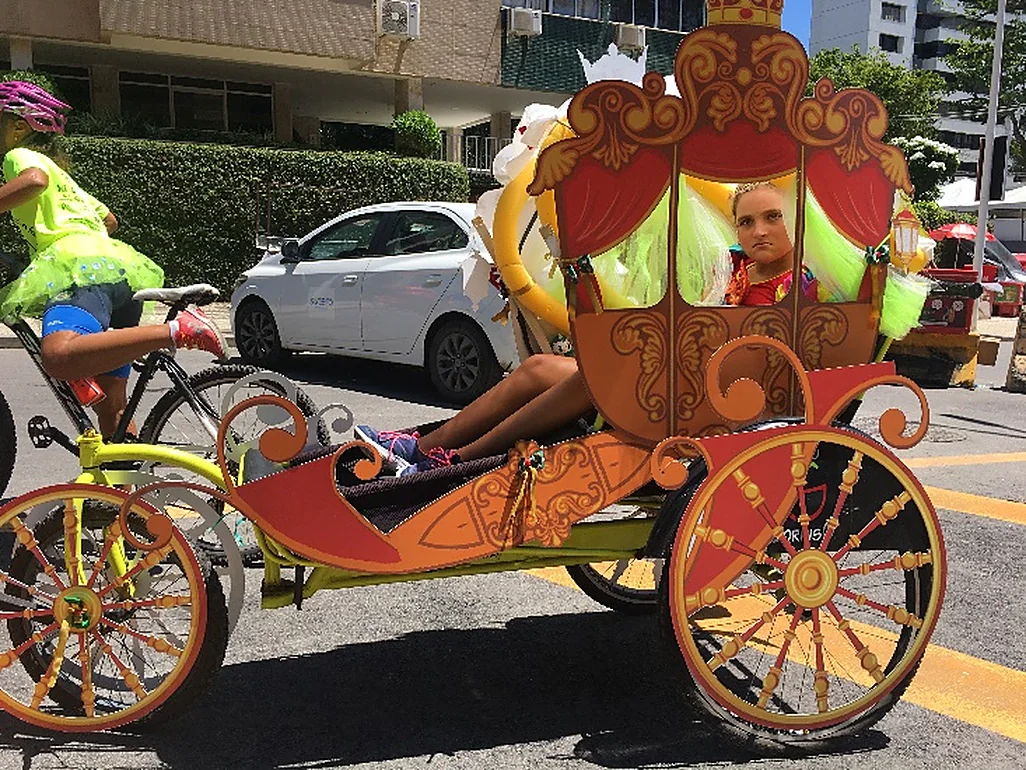 Triciclo ornamentado como uma carruagem dourada leva uma família ao Carnaval.