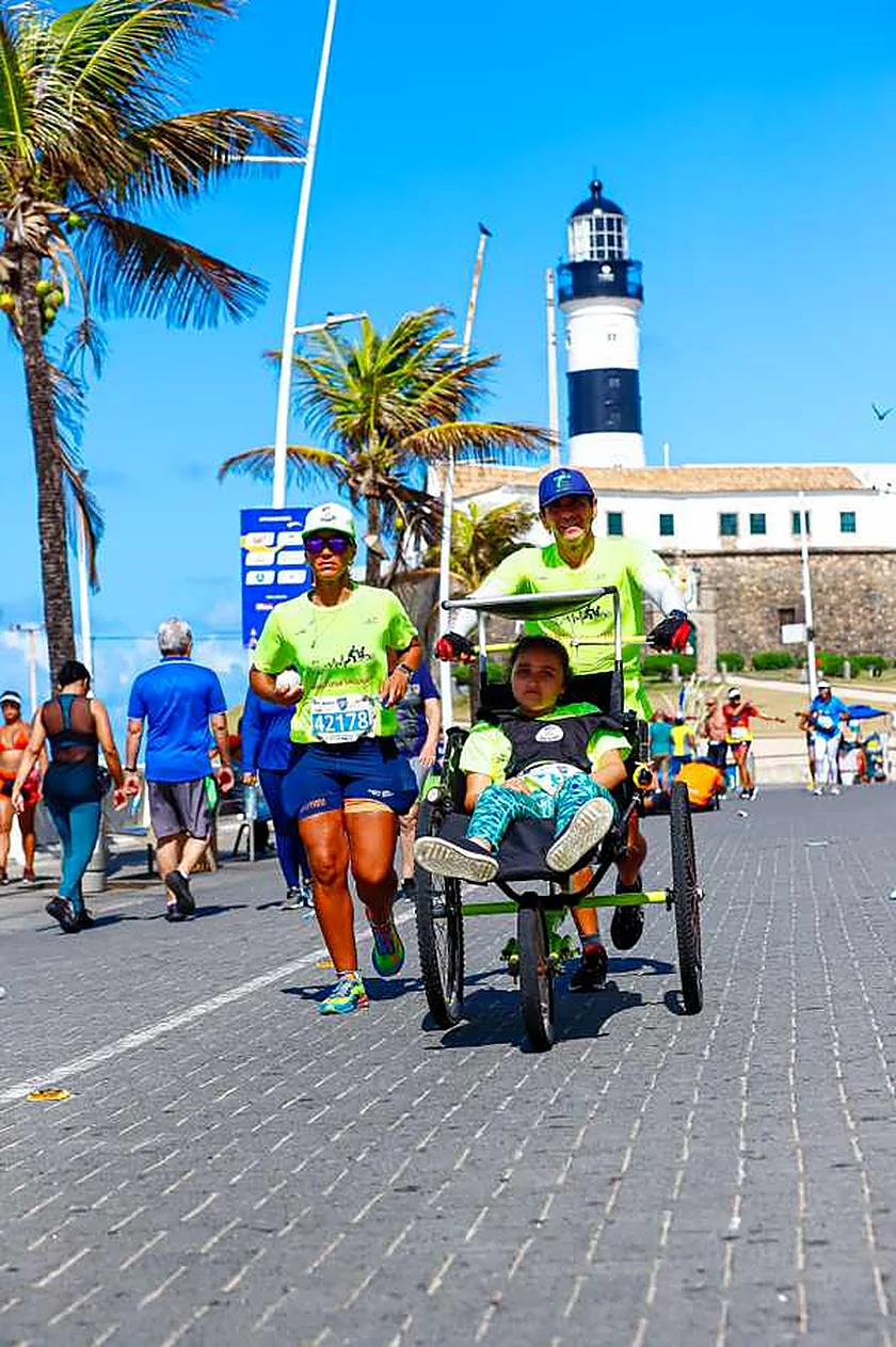 Corredores e um triciclo assistido passam diante do Farol da Barra.