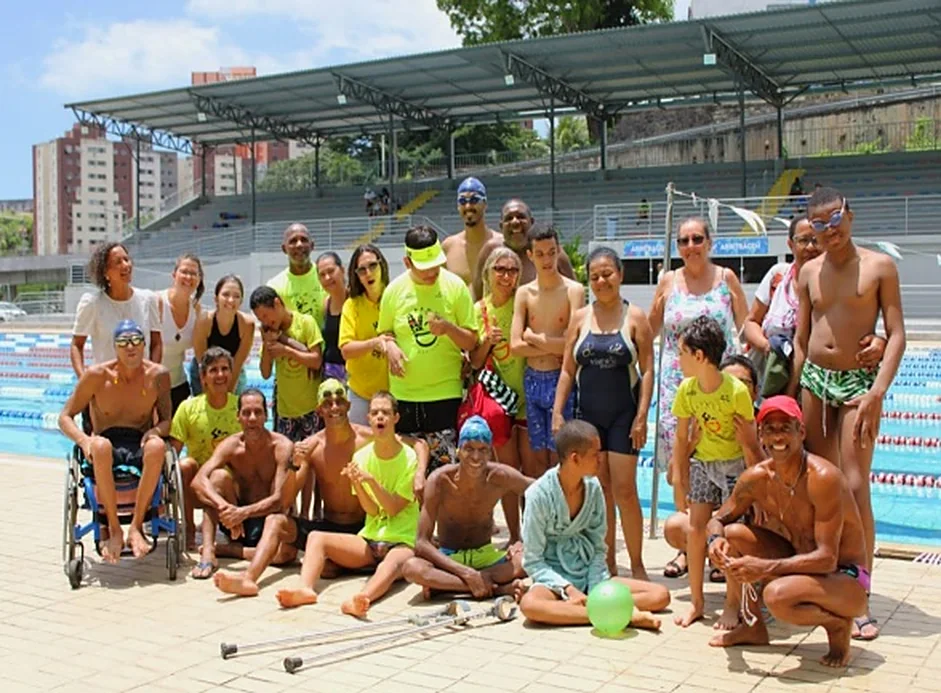 Grupo da natação adaptada reunido à beira da piscina, com cadeiras de rodas e muletas.
