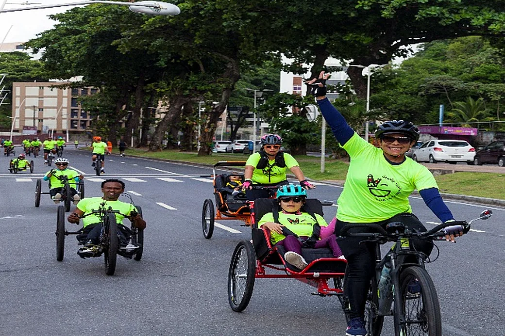 Triciclos assistidos e ciclistas ocupam a avenida fechada para o lazer, uma mulher acena.